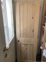 Full view of one solid pine door with arched top panel, 80 inches high, 24 inches wide, leaning against another door.