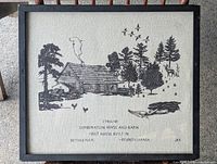 Full view of framed fabric art showing a rustic house with smoke from the chimney, animals, trees and text describing the 1740 Combination House in Bethlehem, PA.