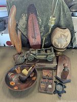 Overview of the group of country home decor items including the wooden bowl, tobacco pipes, antique mouse trap, cast iron turtle holder, thermometer plaque, vintage car model, carved wooden banana, earthenware vase, small wooden stamp holder, and lamp.