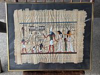Photo showing full framed Egyptian art on beige papyrus with multiple figures and hieroglyphics. The papyrus has natural rough edges and some visible wear on edges.
