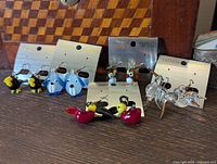 Photo showing multiple pairs of colorful glass animal earrings arranged on earring cards, including black/yellow birds, blue dogs, clear birds, red birds, and owls.