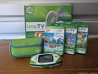 Group of LeapFrog educational video games with handheld console, game cartridges, LeapTV box, and carrying case on wooden surface