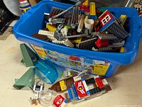 Blue LEGO branded plastic bin filled with assorted LEGO parts including building and vehicle pieces.