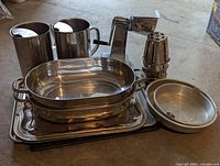 Wide view of large metal serving trays, two drink pitchers, and a grinder with grinding cones and handle.