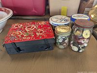 Overall view of two jars filled with old buttons beside an Asian silk embroidered black jewelry box with red floral cover.