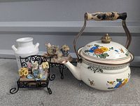 Overview of painted metal teapot, ceramic milk jug, and animal figurines on metal stands, showing group of household decorative items.