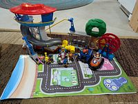Full view of Paw Patrol toys including figures, vehicles, playsets, and play mat spread on carpeted floor.