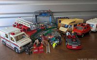 View of large group of Playmobil toys including cars, trucks, figures, and accessories arranged on table.
