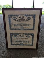 Framed pair of antique stock certificates, showing both certificates in one frame with visible wear and soiling.