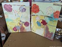 Pair of signed floral art decor paintings showing abstract flowers in various colors with visible light soiling and wear.