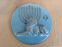 Front view of a round blue plaque showing a lion reclining in front of a menorah and a Star of David.