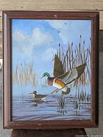 Full front view of the vintage signed wildlife painting framed in wood, showing ducks in flight and swimming in marsh with blue sky background.