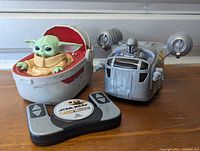 Photo of Baby Yoda figure in floating pod and Mandalorian speeder vehicle with remote control in front