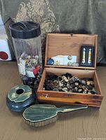 Photo of wood jewelry box filled with vintage buttons, two small tubes of beauty tools in the lid compartment, tall plastic container filled with buttons, and vintage matching hairbrush and decorative container.
