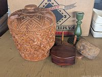Photo showing group of vintage carved wood decor including a large carved lidded jar, dark wooden jewelry box, green candlestick holder, wooden utensils, and stone tool.