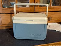Front view of the vintage Coleman cooler showing light blue textured body and white lid embossed with Coleman logo.