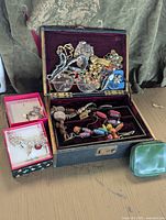 Full view of vintage jewelry box with assorted jewelry inside and two pink Simply Chic boxes containing a ring and bracelet beside it, plus a small green pouch.