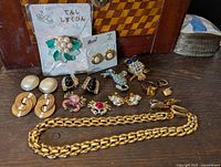 Full group of vintage jewelry including earrings, brooches, rings, chain, and pins displayed on wooden surface