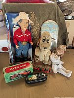 Wide shot showing entire vintage toy group with President Bush doll, mechanical toys, model car, plush toys, and skateboard deck in background.