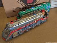 Pair of large vintage metal toy train engines on a wooden surface, with packaging visible behind.