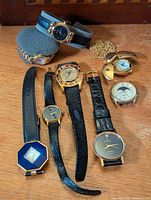 Photo of eight vintage wristwatches and two gold-tone pocket watches on wood surface, showing various dial styles and strap types, including leather and metal bands.