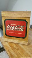 Front view of wooden cabinet featuring Coca Cola logo with phrase 'Drink Coca Cola Delicious and Refreshing'