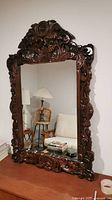 Front view of the large rectangular wooden mirror showing detailed carvings on the frame and reflection of room furniture.