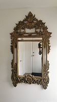 Full front view of rectangular mirror with ornate gold carved frame reflecting hallway door