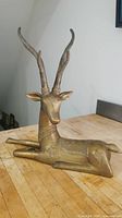 Front-angle photo of brass deer statue on wooden surface, showing intricate ethnic designs and long curved antlers.