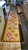 Full length photo of handmade geometric wool runner rug placed in a kitchen, showing the color and pattern in brown, beige, red, and yellow.
