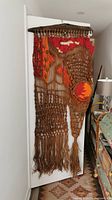 Full view of the large macramé wall hanging displaying earthy color palette, intricate knotting, and wooden rod.