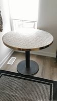Full front view of round marble scalloped tabletop with gold edge and black iron pedestal base
