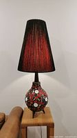 Full view of the tall ceramic mosaic table lamp with switched-on light showing the lamp shade illuminated in warm red and black colors.
