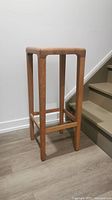 Side view of oak bar stool with simple rectangular design and footrest supports.