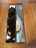 Seven dark brown wavy hair extension pieces arranged in original packaging on a wood surface, showing length and color of the extensions.