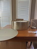 Pendant light fixture with a gold/brass perforated metal drum shade, diffuser plate, and mounting components on a wooden table.