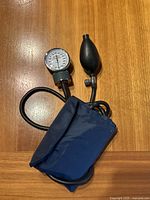Manual blood pressure pump showing black rubber bulb, attached gauge with dial, and navy blue fabric cuff.