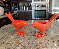 Pair of orange ceramic bird-shaped tealight candle holders shown standing on a granite countertop in a kitchen setting.