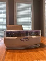 Front view of Conair Big Curls heated hair curler set with clear plastic cover on a wooden table