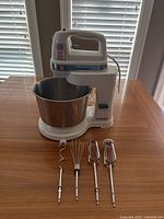Cuisinart hand and stand mixer setup with stainless steel mixing bowl on wooden table, showing power cord and name branding on device.
