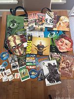 Overview of entire lot showing bags, comic books, posters, pins, stickers, and mask.