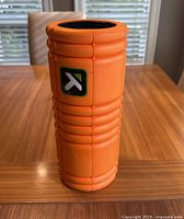 Orange TriggerPoint foam roller standing upright on wooden table.