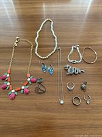 Photo shows assorted jewelry arranged on a wooden surface, including necklaces, rings, bracelets, brooches, and earrings.