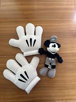 Front view of black and white vintage-style Mickey Mouse plush doll with two oversized plush Mickey Mouse gloves on wooden surface