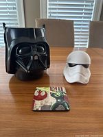 Photo showing Darth Vader pail, Stormtrooper head collectible, and Luke Skywalker coaster on a table with window blinds in the background.