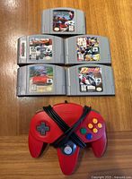 Top view showing five Nintendo 64 game cartridges arranged in a pyramid formation with a red Nintendo 64 controller in front. All game labels are clearly visible.