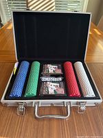 Open aluminum case showing poker chips in blue, green, red, white and black colors, two decks of Texas Hold'em playing cards, and five white dice