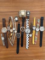 Full layout showing all 12 wristwatches and 1 wide cuff watch bracelet on wooden surface