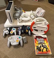 White Wii console upright with power adapter connected, Nunchuks, sensor bar, charging dock and cables on platform