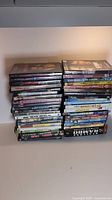 Photo of approximately 45 DVDs stacked in two piles showing titles and cases in good used condition.